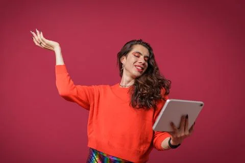 Non-binary person using a tablet on a red background and wearing pride clothi Stock Photos