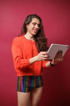 Non-binary person using a tablet on a red background and wearing pride clothi Stock Photos