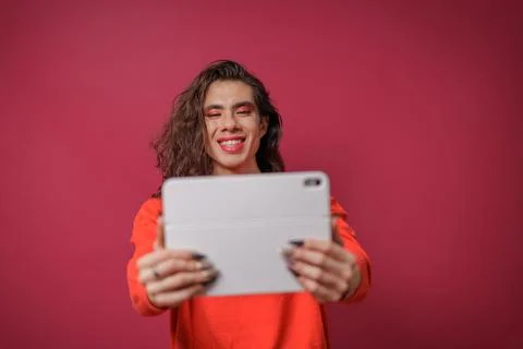 Non-binary person using a tablet on a red background and wearing pride clothi Stock Photos