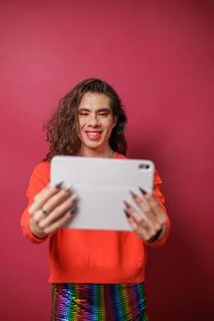 Non-binary person using a tablet on a red background and wearing pride clothi Stock Photos
