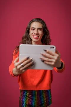 Non-binary person using a tablet on a red background and wearing pride clothi Stock Photos
