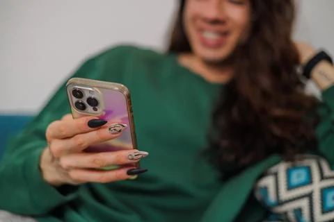 Non-binary person using their cell phone at home with blurred background. L.. Stock Photos