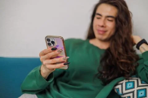 Non-binary person using their cell phone at home with blurred background. L.. Stock Photos