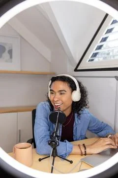 Non-binary podcaster wearing denim shirt using microphone at converted attic Stock Photos