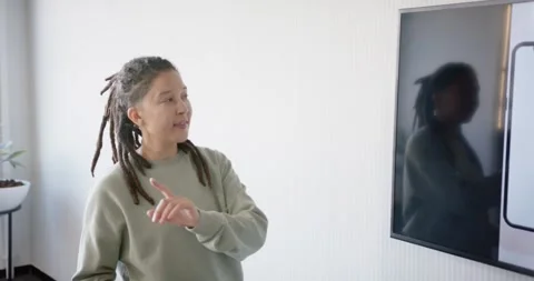 Non-binary presenter in green sweatshirt starting demo, pointing at smartphone Stock Footage 344673181