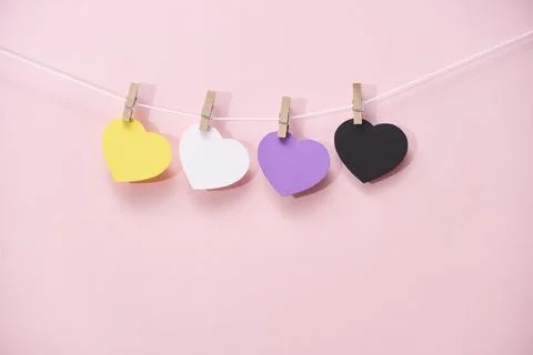 Non binary pride flag paper hearts hanging on string over pink background Foto stock