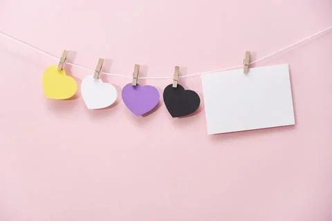 Non binary pride flag paper hearts hanging on string over pink background Foto stock