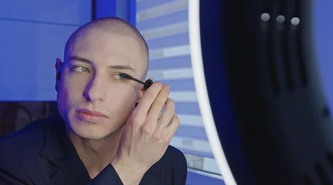 Non-binary queer person prepares themselves to go out and puts mascara on Stock Photos
