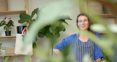 Non-binary seller in apron in plant shop greeting clients while camera pulling Stock Footage 339559476