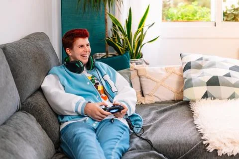 Non-binary smiling person playing video games in the living room at home Stock Photos