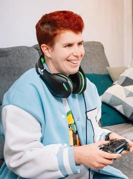 Non-binary smiling person playing video games in the living room at home Stock Photos