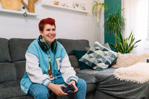 Non-binary smiling person playing video games in the living room at home Stock Photos