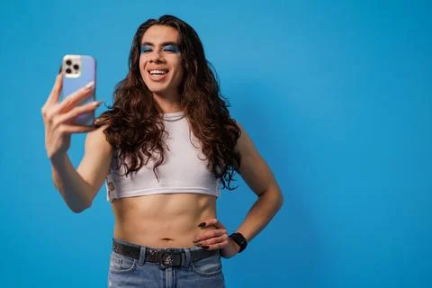Non-binary stylish person taking a photo with their cell phone on a blue back Stock Photos