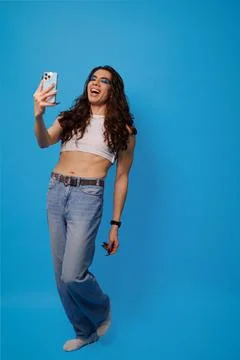 Non-binary stylish person taking a photo with their cell phone on a blue back Stock Photos
