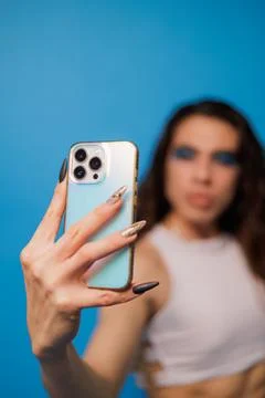 Non-binary stylish person taking a photo with their cell phone on a nice blue Stock Photos