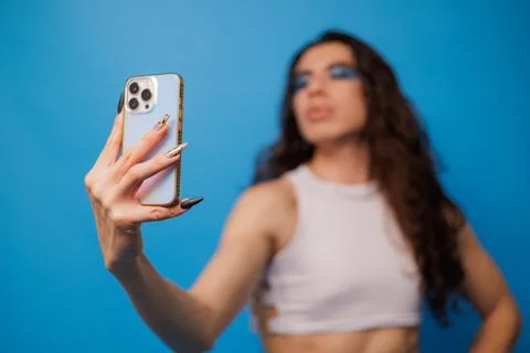 Non-binary stylish person taking a photo with their cell phone on a nice blue Stock Photos