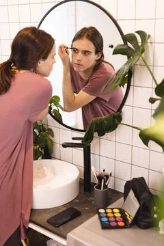 Non-binary trans woman doing her eyebrow makeup looking in the mirror in Stock Photos