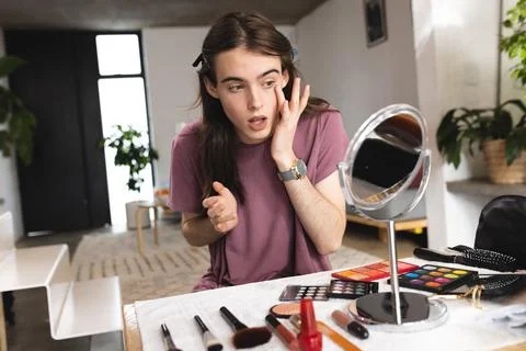 Non-binary trans woman doing makeup looking in the makeup mirror at home Stock Photos