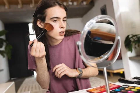 Non-binary trans woman doing makeup with blusher brush looking in the makeup Stock Photos