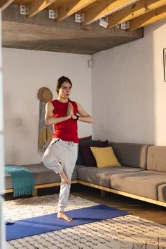 Non-binary trans woman practicing yoga and meditation standing on yoga mat at Stock Photos