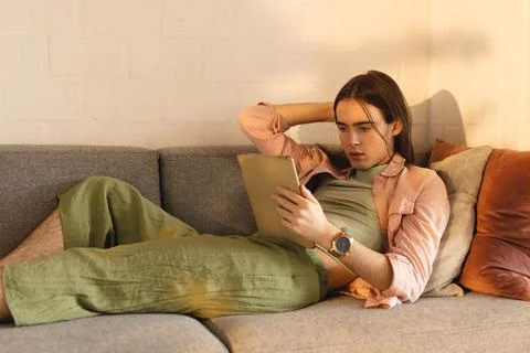 Non-binary trans woman using digital tablet lying on the couch at home Stock Photos
