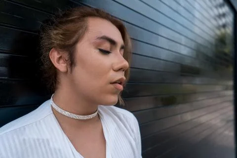 Non-binary using phone in her hands chating leaning on black gate in the street Stock Photos