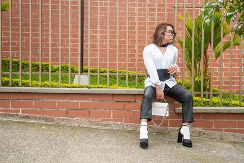 Non-binary vain man dressing corset and purse leaning on black gate in the Stock Photos