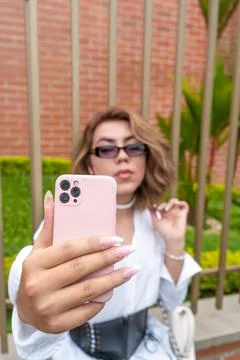 Non-binary vain man taking selfie leaning on black gate in the street Stock Photos