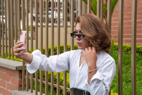 Non-binary vain man taking selfie leaning on black gate in the street Stock Photos