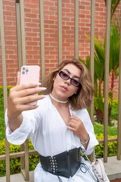 Non-binary vain man taking selfie leaning on black gate in the street Stock Photos