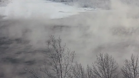 Non-freezing river flows among snowy shores, steam rises from water, winter Stock Footage 128979111