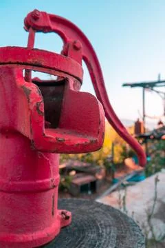 Non-functioning old fashioned red water pump on wooden block. Stock Photos