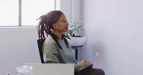 Nonbinary adult wearing green top seated in office chair holding paper listening Stock Footage 345820547