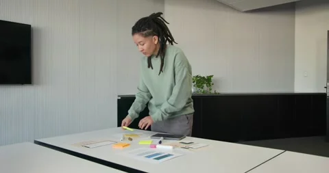 Nonbinary African American reading sticky note arranging neon pads and tablet at Stock Footage 342033162