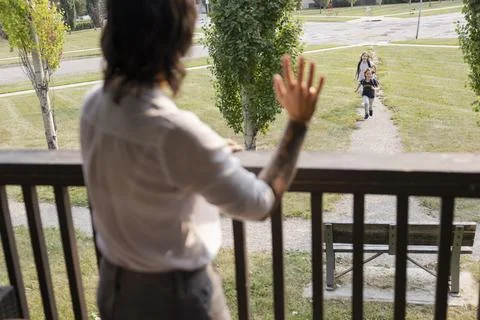 Nonbinary parent waving to kids returning home from school Stock Photos