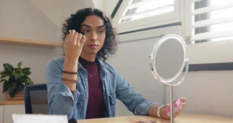 Nonbinary person loading powder brush, blending makeup, checking mirror at desk Stock Footage 338167516