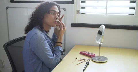 Nonbinary person opening palette at desk applying concealer and blush while Stock Footage 344104353