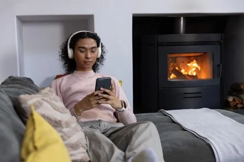Nonbinary person reclining on gray sofa in cozy living room, wearing pink Stock Photos