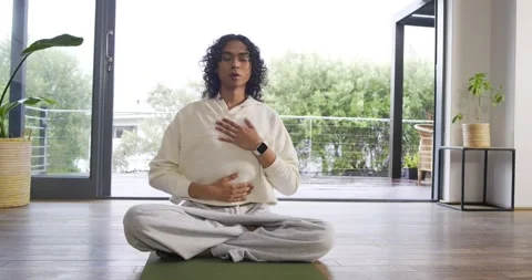 Nonbinary person settling on yoga mat in living room near balcony practicing Stock Footage 341467273