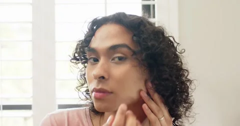 Nonbinary person styling hair massaging cheeks starting day at vanity by white Stock Footage 335927153