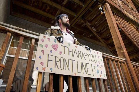 Nonbinary person thanking frontline workers with sign on balcony Foto stock