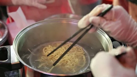 Noodles are being boiled while being stirred with chopsticks Stock Footage 272298299