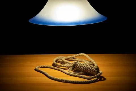 A noose lying on the table under a glowing chandelier, on a black background Stock Photos