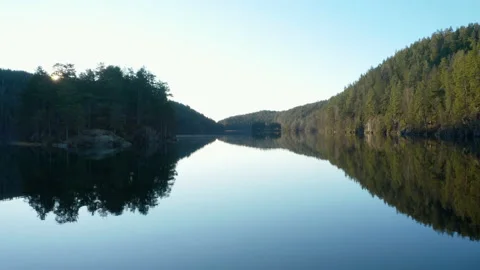 Nordic lake, blue sky reflection mirror, fly low revealing morning sun over tree Stock Footage 149618271