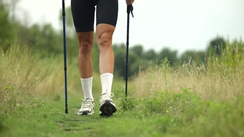 Nordic walker performing marching exercise with trekking poles on grassy trail Stock Footage 313951309