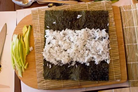 Nori algae leaf with rice for rolls with cucumber and avocado on a wooden boa Stock Photos