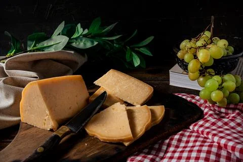 A Normal view of a piece of provolone cheese cut on a board and some grapes i Stock Photos