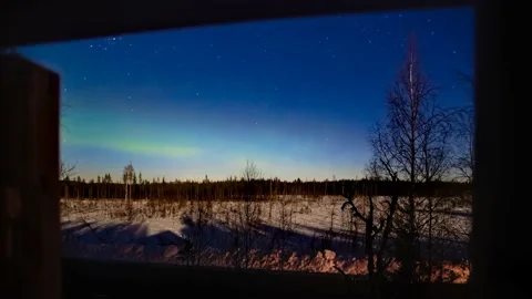 Northern lights until dawn over moonlit winter landscape, shot through a window Stock Footage 155555516