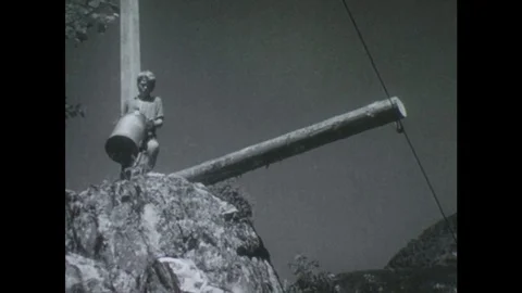 NORWAY 1950s: Low angle shot, boy carries jug to cliff edge / Boy attaches jug Vidéo 75229484