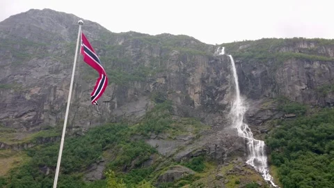 A Norwegian Flag Fluttering by Wind With A Glacier Waterfall in The Background. Video stock 305094441